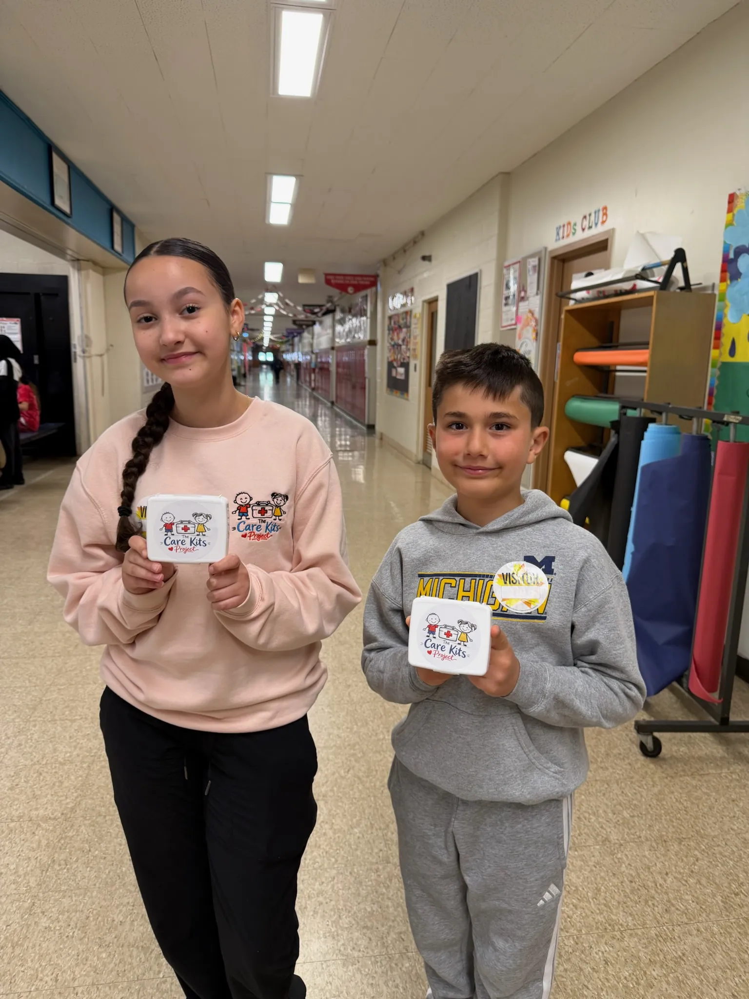 Two students in a school hallway, each holding up the care kit they built