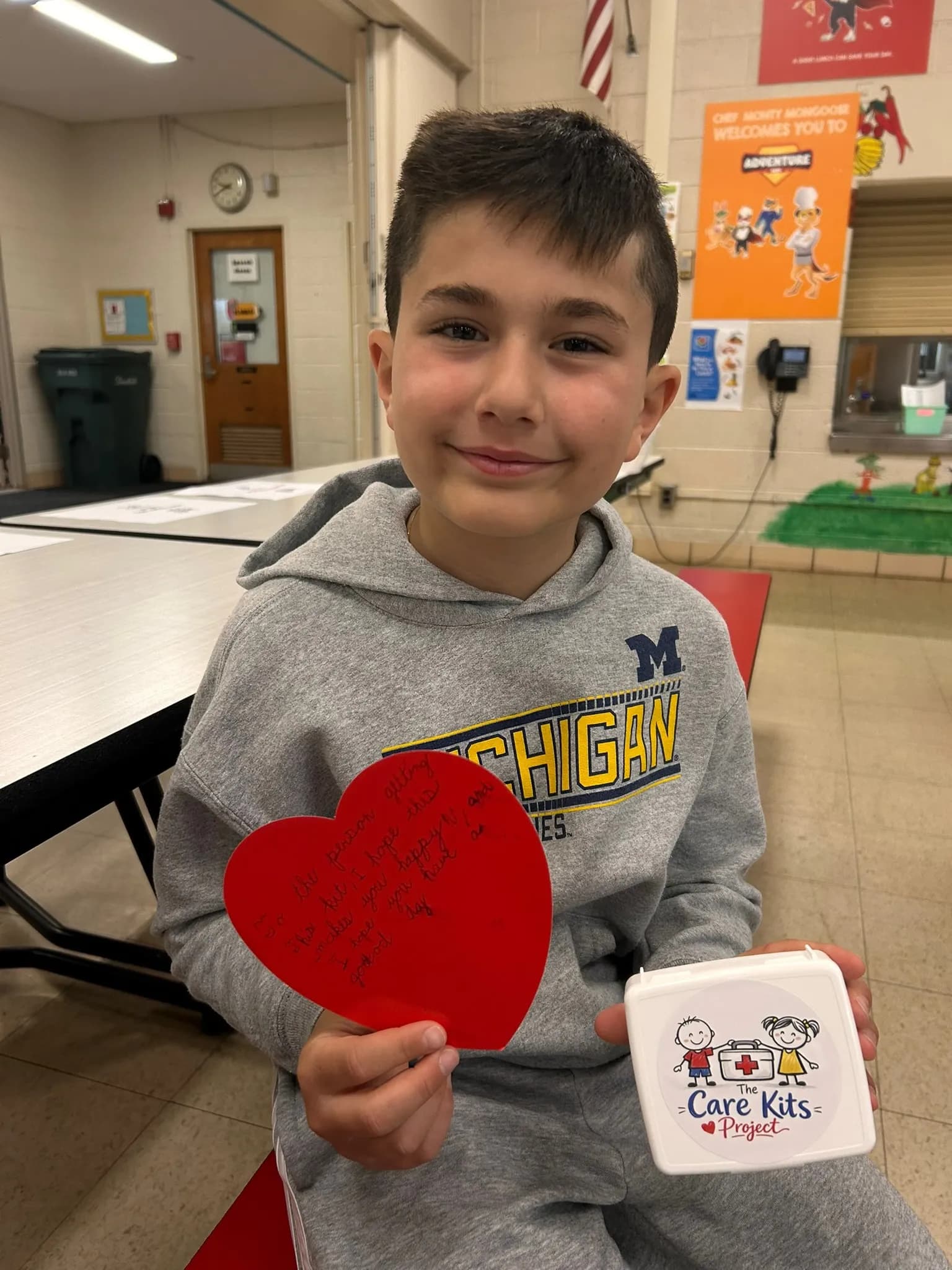 A student holding a handwritten heart note and his care kit