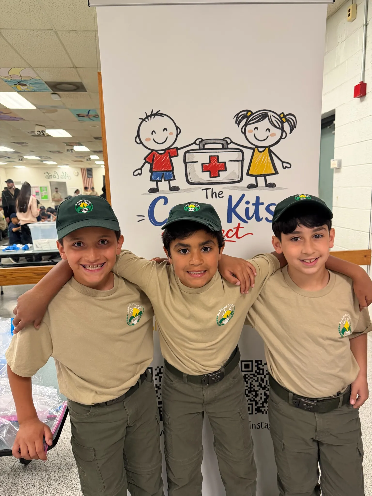 Three young scouts smiling in front of the Care Kits Project banner